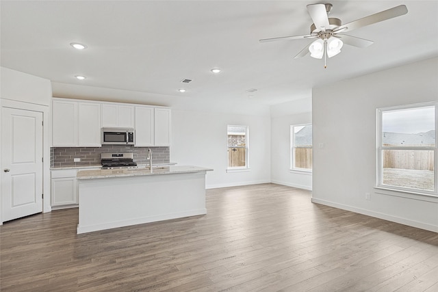 kitchen with a kitchen island with sink, stainless steel appliances, wood finished floors, white cabinets, and backsplash