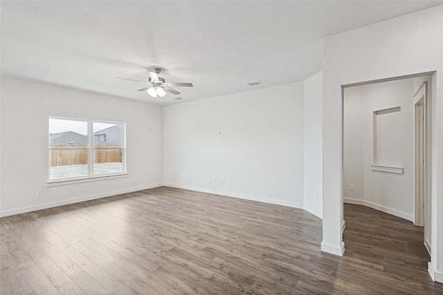 unfurnished room with dark wood-style floors, baseboards, visible vents, and a ceiling fan