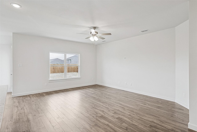 empty room with a ceiling fan, wood finished floors, visible vents, and baseboards