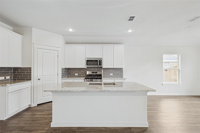 kitchen featuring appliances with stainless steel finishes, white cabinetry, light stone counters, and an island with sink