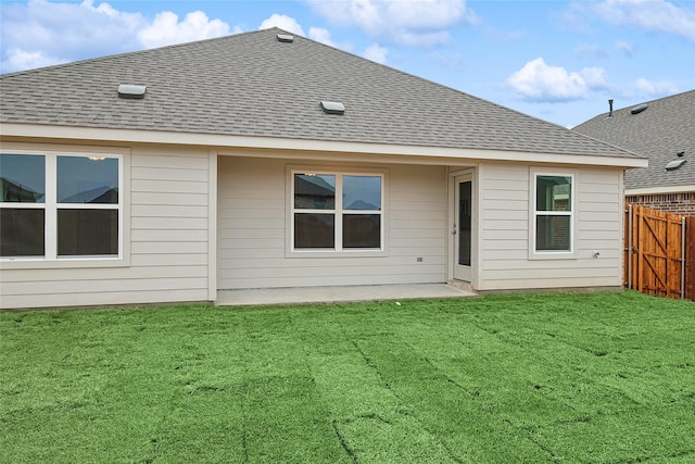 rear view of property featuring a yard, a shingled roof, and fence