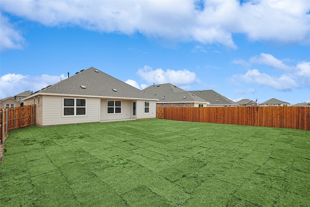 back of property with a yard, roof with shingles, and a fenced backyard