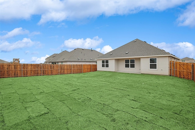 rear view of property featuring roof with shingles, a lawn, and a fenced backyard