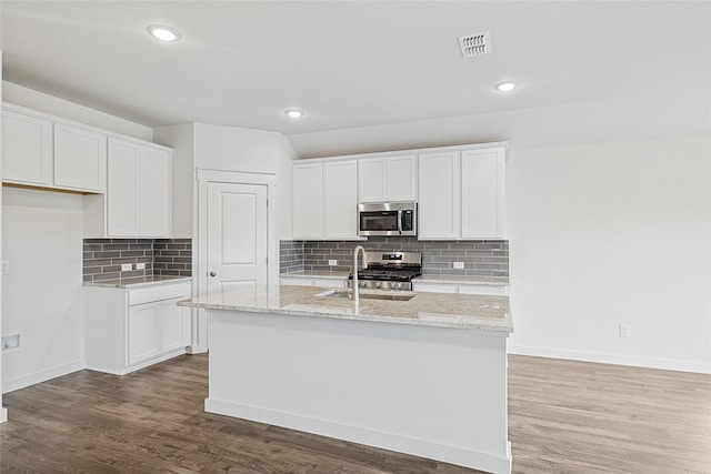 kitchen with a center island with sink, visible vents, appliances with stainless steel finishes, white cabinetry, and wood finished floors