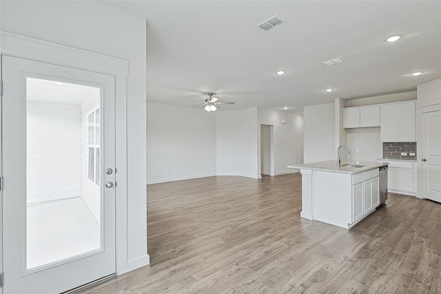 kitchen with a sink, visible vents, white cabinets, light countertops, and an island with sink