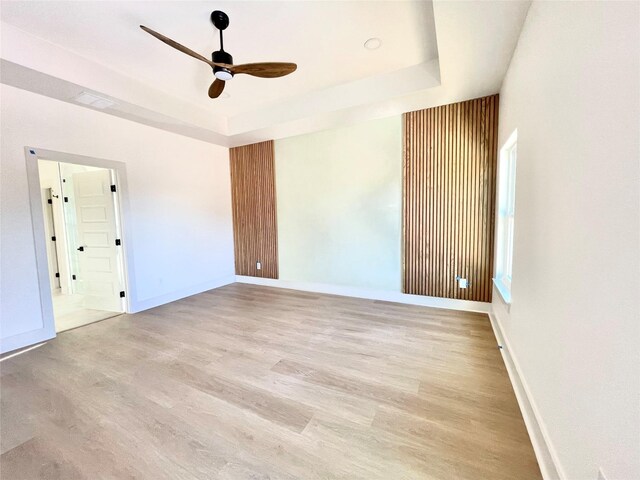 unfurnished room with light hardwood / wood-style flooring, a raised ceiling, and ceiling fan