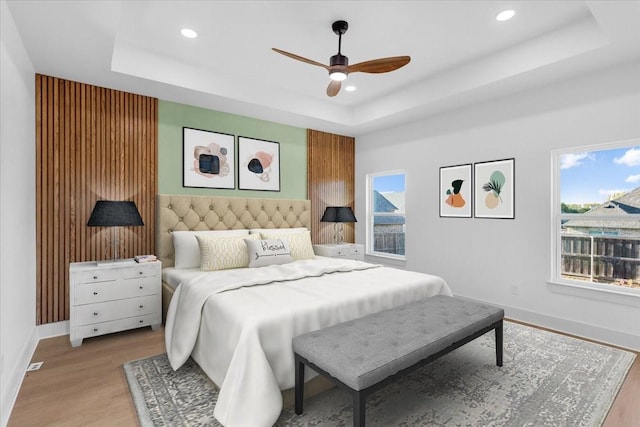 bedroom with ceiling fan, a raised ceiling, and light wood-type flooring