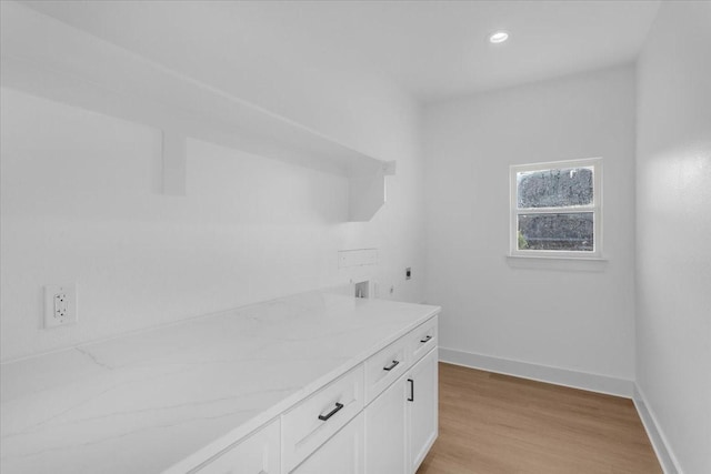 laundry room with hookup for an electric dryer, light hardwood / wood-style flooring, and cabinets