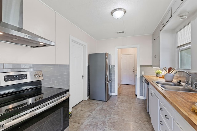 kitchen with stainless steel appliances, wall chimney range hood, white cabinets, and wood counters