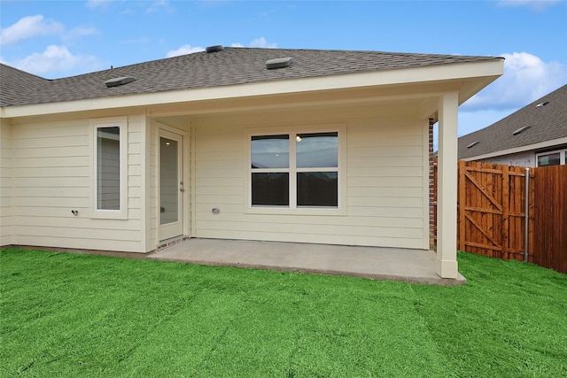 rear view of house with roof with shingles, fence, and a lawn