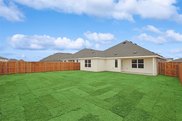 rear view of house with a fenced backyard, a yard, and roof with shingles