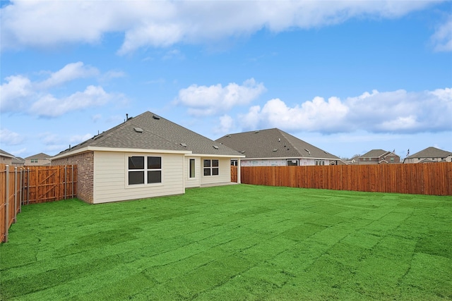 rear view of property featuring a fenced backyard, a lawn, brick siding, and roof with shingles