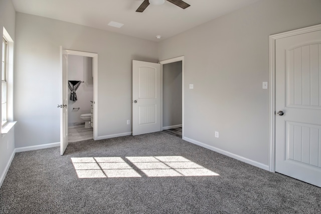 unfurnished bedroom featuring ceiling fan, dark carpet, and ensuite bath