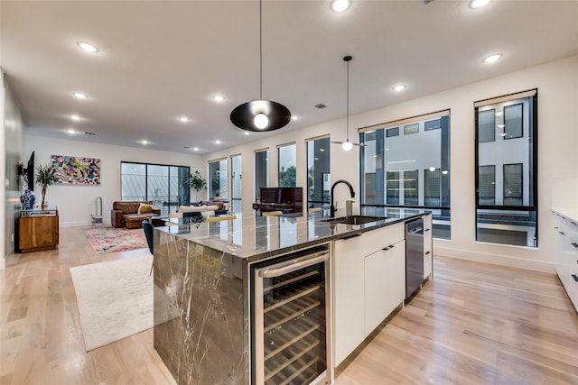 kitchen featuring pendant lighting, white cabinetry, an island with sink, and wine cooler