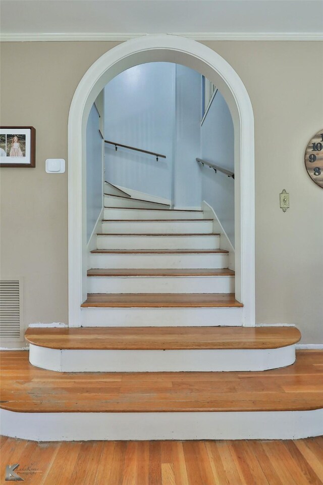 stairway with wood-type flooring and crown molding