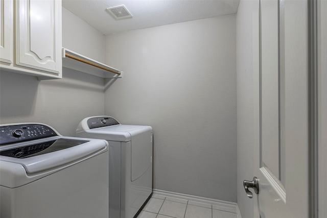 laundry room with cabinets, light tile patterned flooring, a textured ceiling, and washer and clothes dryer