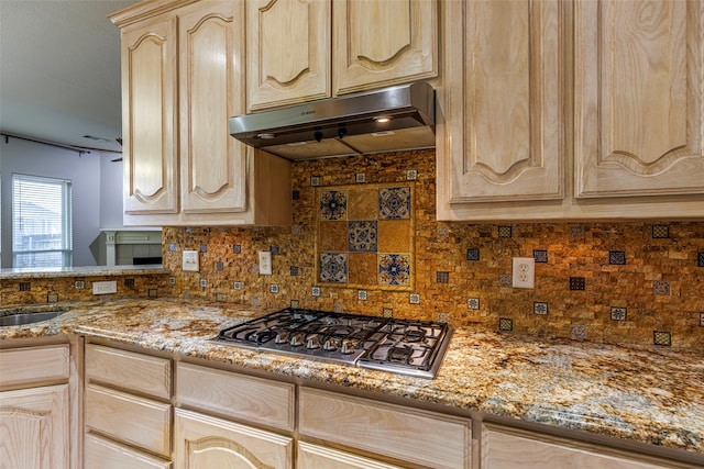 kitchen with tasteful backsplash, light brown cabinetry, light stone countertops, stainless steel gas stovetop, and exhaust hood