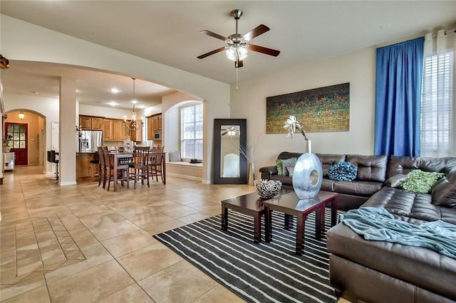 tiled living room with ceiling fan with notable chandelier