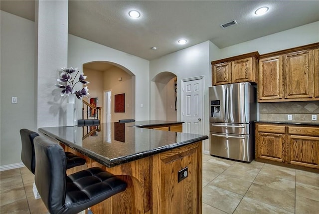 kitchen with dark stone countertops, stainless steel fridge, a kitchen bar, decorative backsplash, and a kitchen island