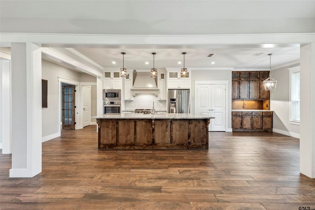 kitchen with appliances with stainless steel finishes, tasteful backsplash, custom exhaust hood, decorative light fixtures, and a spacious island