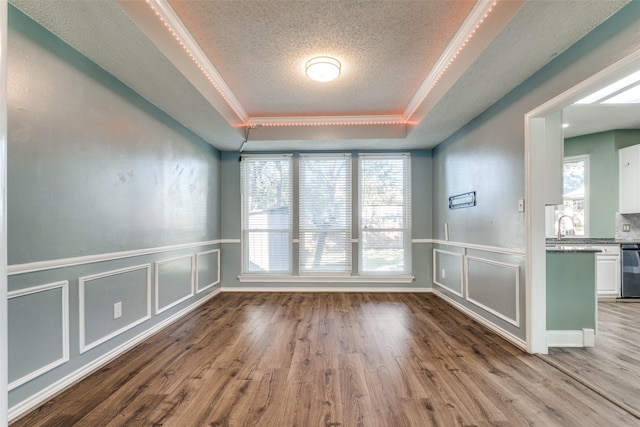 spare room featuring ornamental molding, a tray ceiling, a textured ceiling, and light wood-type flooring