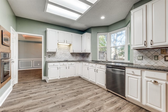 kitchen with appliances with stainless steel finishes, white cabinetry, sink, dark stone countertops, and light wood-type flooring