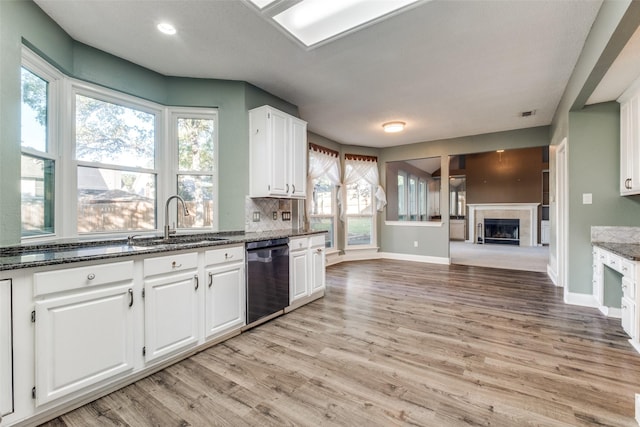 kitchen with dishwashing machine, sink, dark stone countertops, white cabinets, and a tiled fireplace