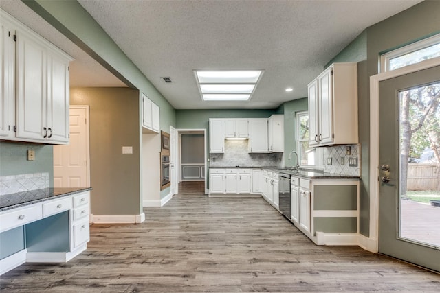 kitchen featuring dark stone countertops, appliances with stainless steel finishes, a skylight, and white cabinets