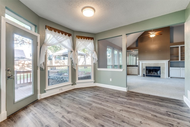 unfurnished living room featuring ceiling fan, a tile fireplace, a textured ceiling, and a wealth of natural light