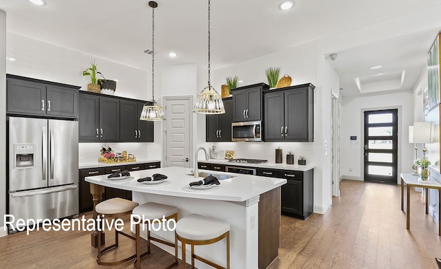 kitchen featuring stainless steel appliances, wood-type flooring, a center island with sink, hanging light fixtures, and a kitchen breakfast bar