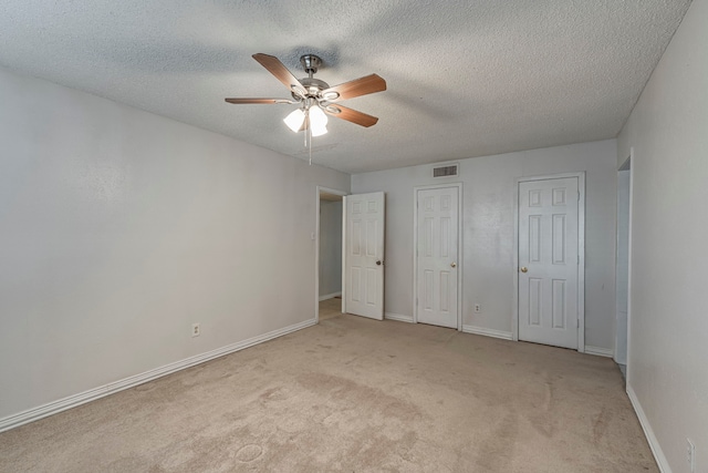 unfurnished bedroom featuring ceiling fan, light colored carpet, a textured ceiling, and two closets