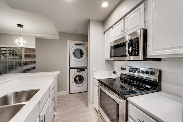 kitchen featuring light hardwood / wood-style floors, appliances with stainless steel finishes, hanging light fixtures, white cabinets, and stacked washer and dryer