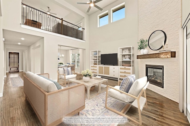 living room with ceiling fan with notable chandelier, a large fireplace, baseboards, and wood finished floors