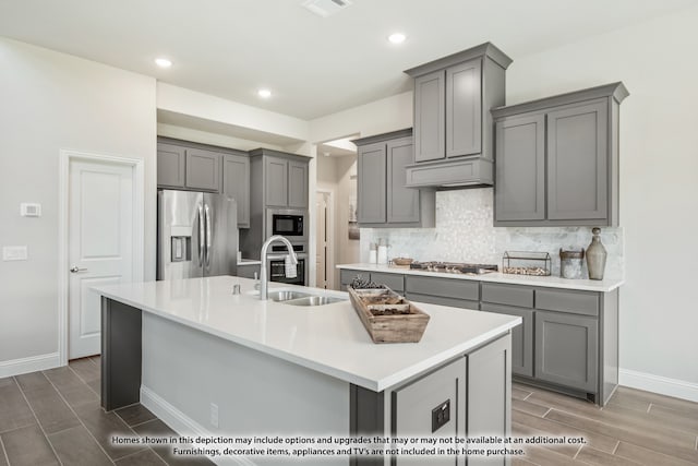 kitchen with gray cabinets, appliances with stainless steel finishes, and an island with sink