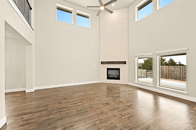 unfurnished living room featuring a large fireplace, a healthy amount of sunlight, baseboards, and dark wood-style flooring