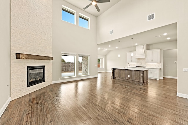 unfurnished living room with a stone fireplace, dark wood-type flooring, visible vents, and a ceiling fan