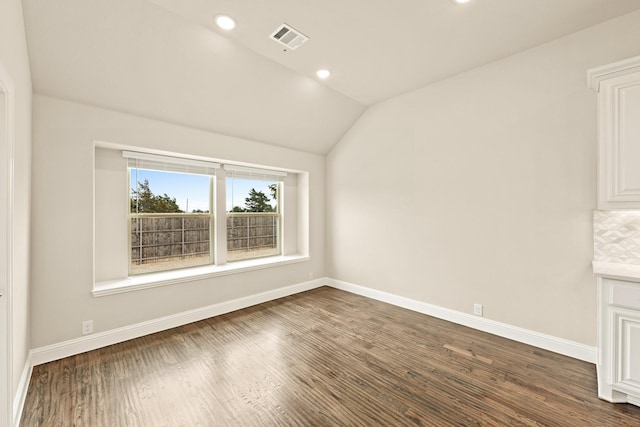 empty room with vaulted ceiling, dark wood-type flooring, visible vents, and baseboards