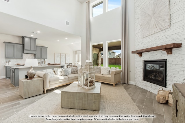 living room featuring a high ceiling, a stone fireplace, and light hardwood / wood-style flooring