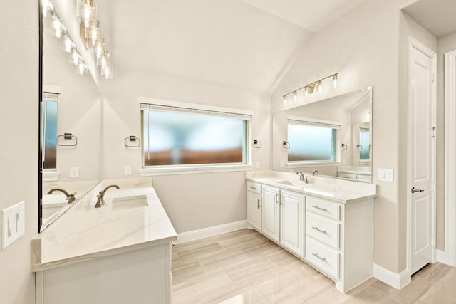 full bathroom with lofted ceiling, two vanities, a sink, and baseboards