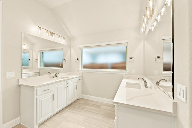 full bath featuring vaulted ceiling, two vanities, a sink, and baseboards