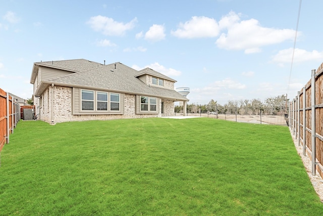 back of property with a yard, a shingled roof, a fenced backyard, and brick siding