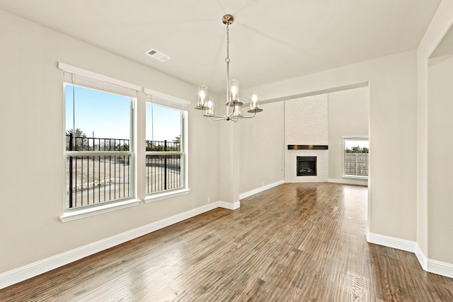 unfurnished living room with a chandelier, a fireplace, wood finished floors, visible vents, and baseboards