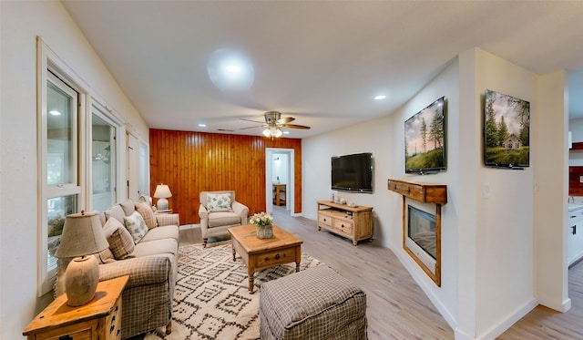 living room with ceiling fan, wooden walls, and light hardwood / wood-style floors