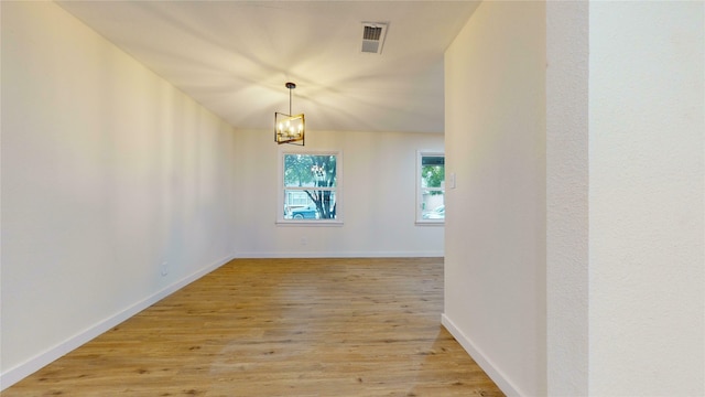 spare room featuring a chandelier and light wood-type flooring