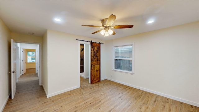 unfurnished bedroom with light hardwood / wood-style flooring, a barn door, and ceiling fan