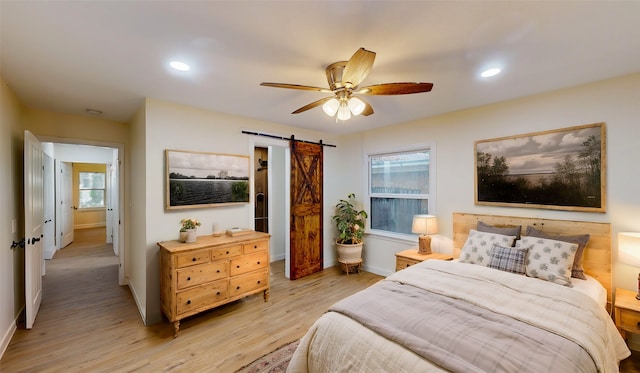 bedroom featuring ceiling fan, a barn door, and light hardwood / wood-style floors