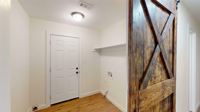 laundry room with hookup for a washing machine, a barn door, and light wood-type flooring