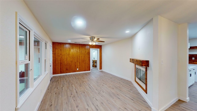 unfurnished living room with wood walls, ceiling fan, and light hardwood / wood-style flooring