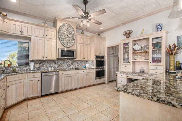 kitchen featuring appliances with stainless steel finishes, ornamental molding, dark stone counters, sink, and light tile patterned floors