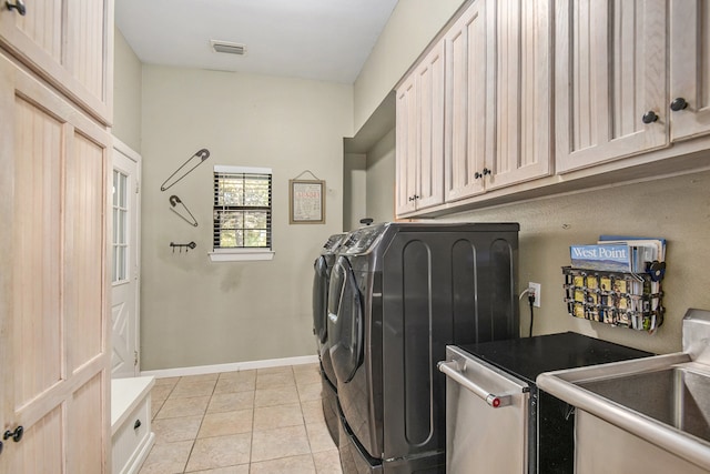 clothes washing area with washing machine and dryer, sink, light tile patterned floors, and cabinets